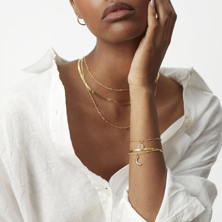 model in white shirt wearing a gold bead chain choker necklace, layered with a flat snake chain necklace in gold and a gold figaro chain necklace